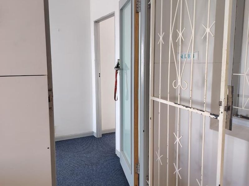 A functional office hallway featuring a security gate, carpeted flooring, and access to multiple internal rooms.