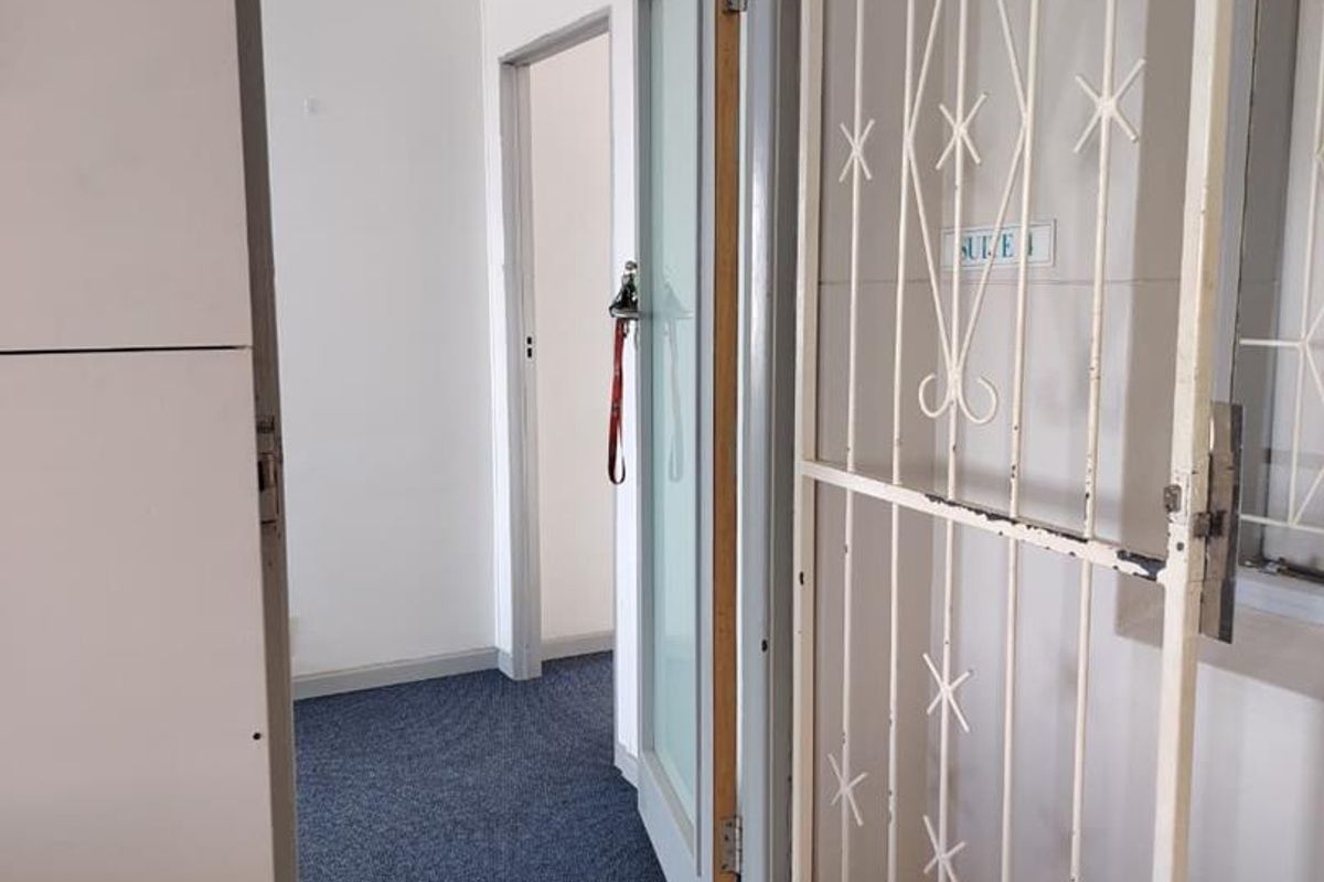 A functional office hallway featuring a security gate, carpeted flooring, and access to multiple internal rooms.