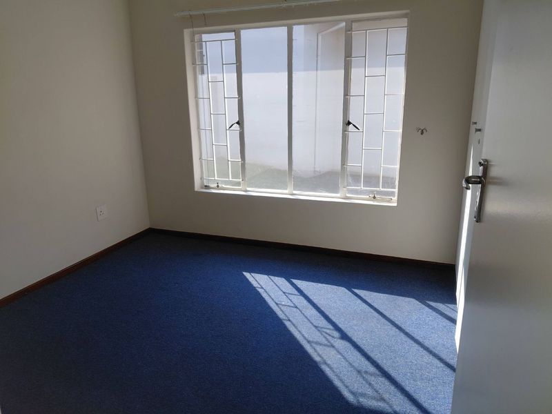 An empty bedroom featuring blue carpeting, neutral walls, and a window fitted with security bars.