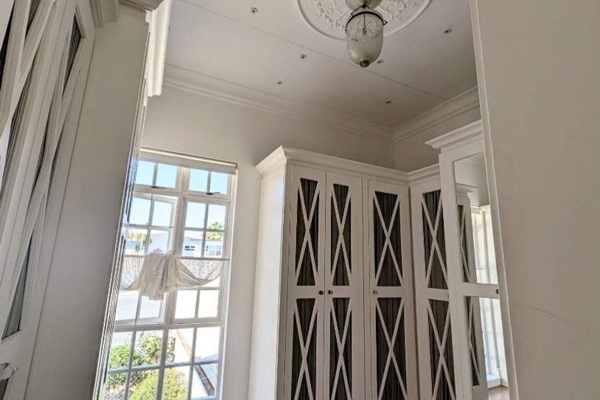 A bright bedroom featuring elegant built-in cabinetry, a decorative ceiling rose, recessed lighting, and large multi-pane windows with wood-look flooring.