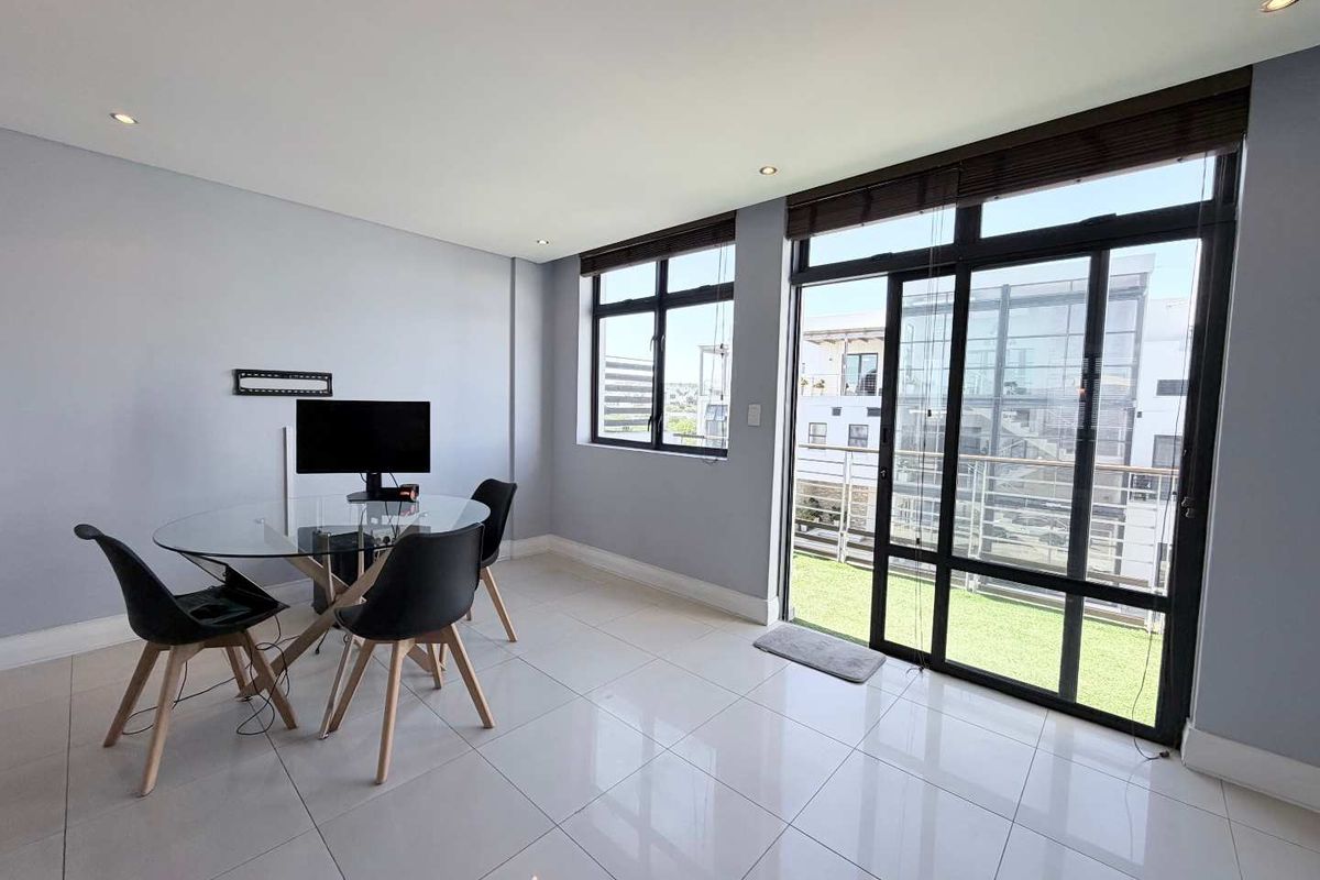Bright living area featuring large aluminium framed windows and sliding doors leading to a balcony, finished with modern tiled flooring and recessed lighting.
