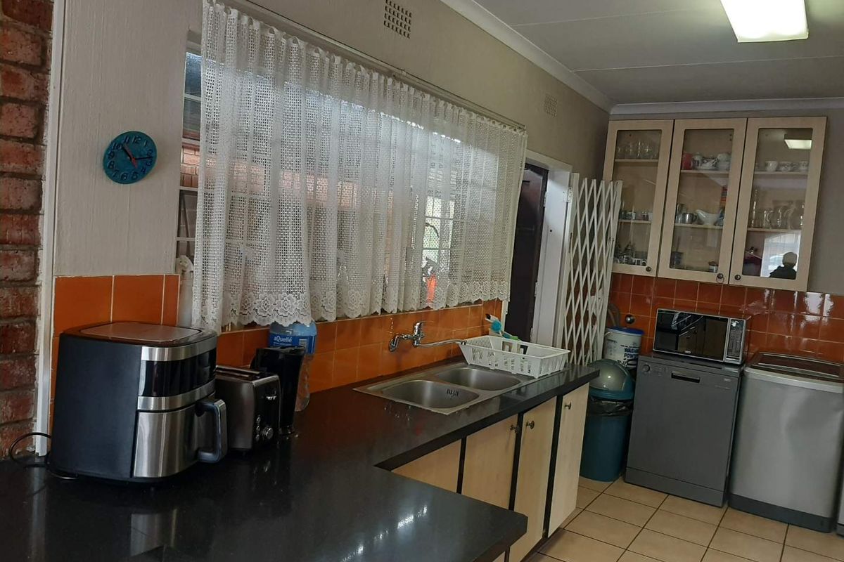 Functional kitchen featuring dark countertops, double stainless steel sink, built-in cabinetry, and orange tiled splashbacks.