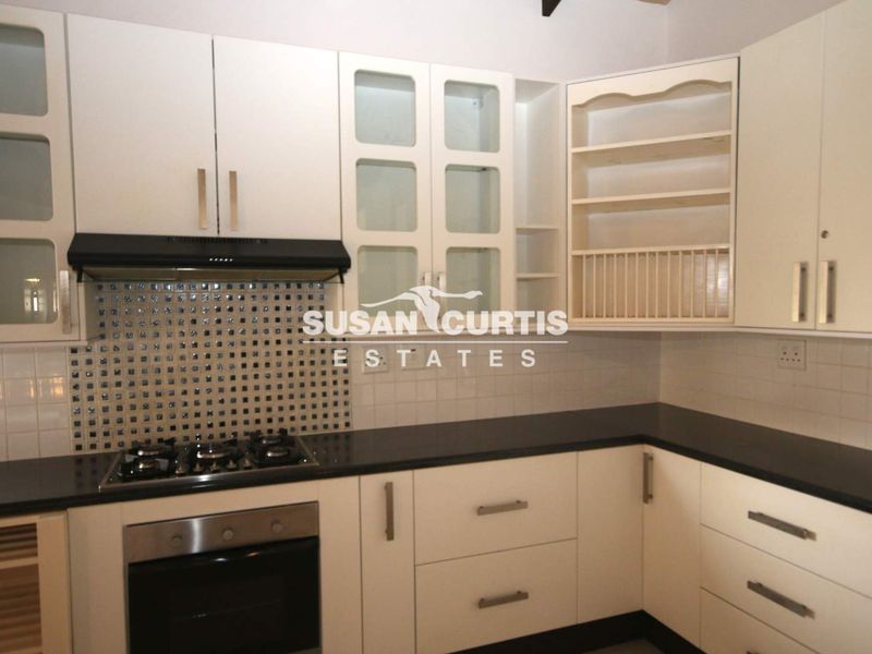 A functional kitchen featuring cream-colored cabinetry, dark stone countertops, a gas hob with extractor fan, and a decorative mosaic tile backsplash.