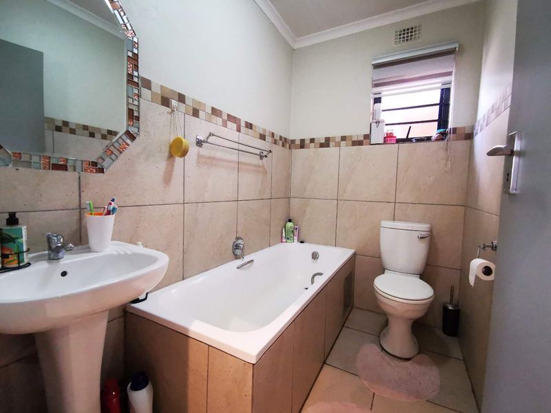 A functional bathroom featuring a pedestal basin, built-in bathtub, and toilet with neutral wall and floor tiling.