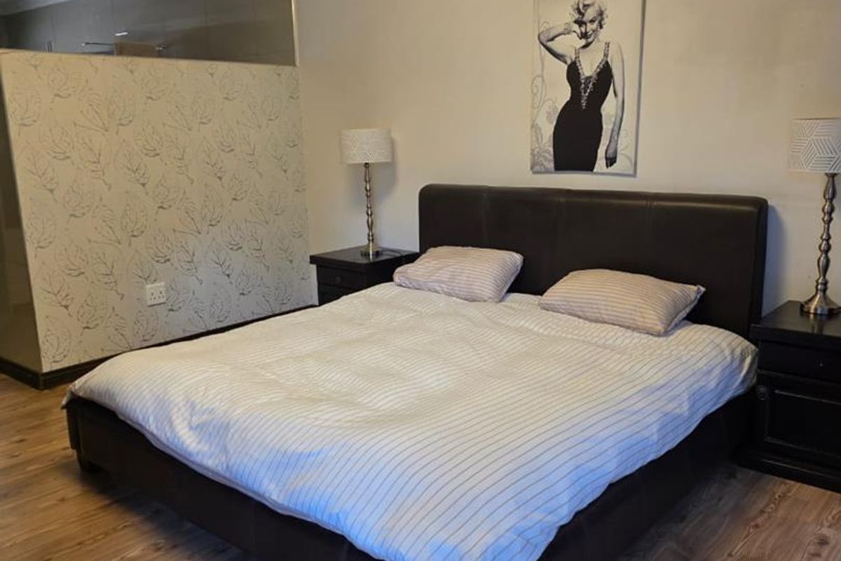 A bedroom featuring laminate flooring, a textured ceiling, and a partial room divider wall.