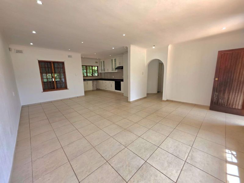 Spacious open-plan living area featuring tiled flooring, recessed lighting, and a functional kitchen with built-in cabinetry and appliances.