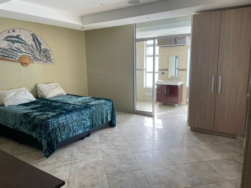 Spacious bedroom featuring tiled flooring, built-in wardrobe, and direct access to an en-suite bathroom through a sliding glass door.
