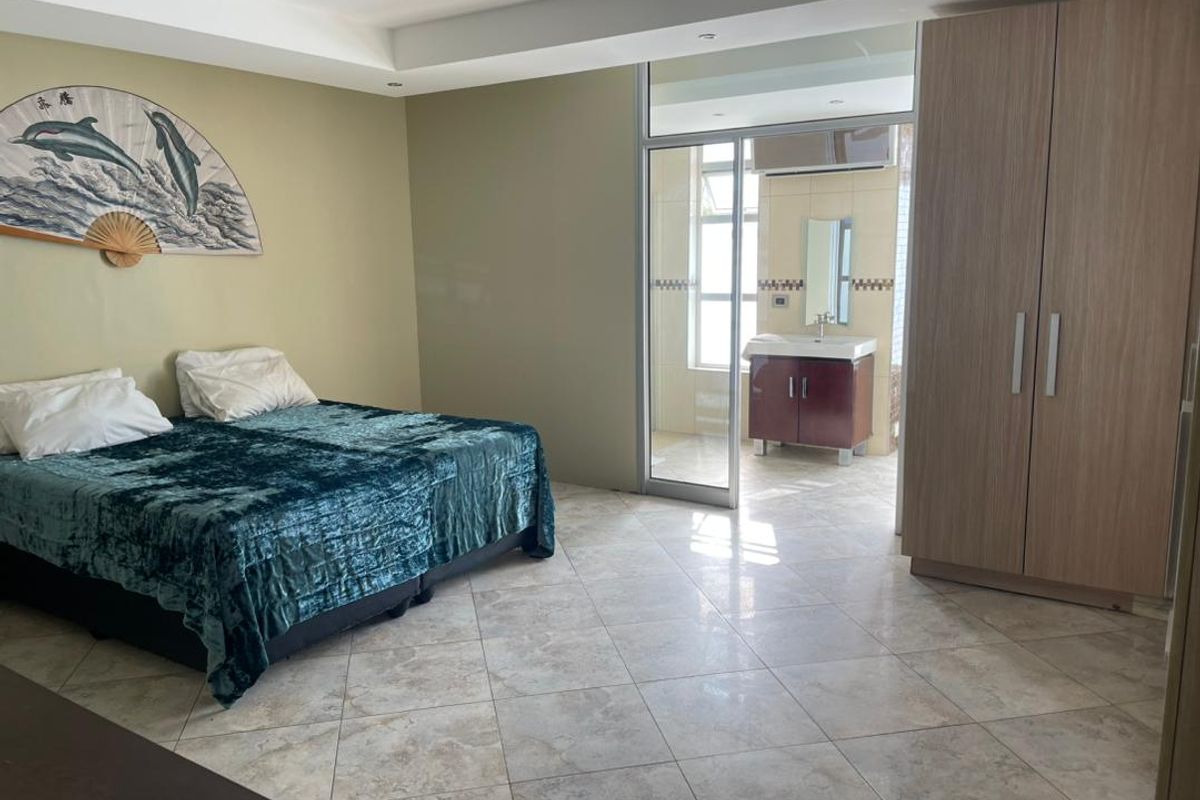 Spacious bedroom featuring tiled flooring, built-in wardrobe, and direct access to an en-suite bathroom through a sliding glass door.