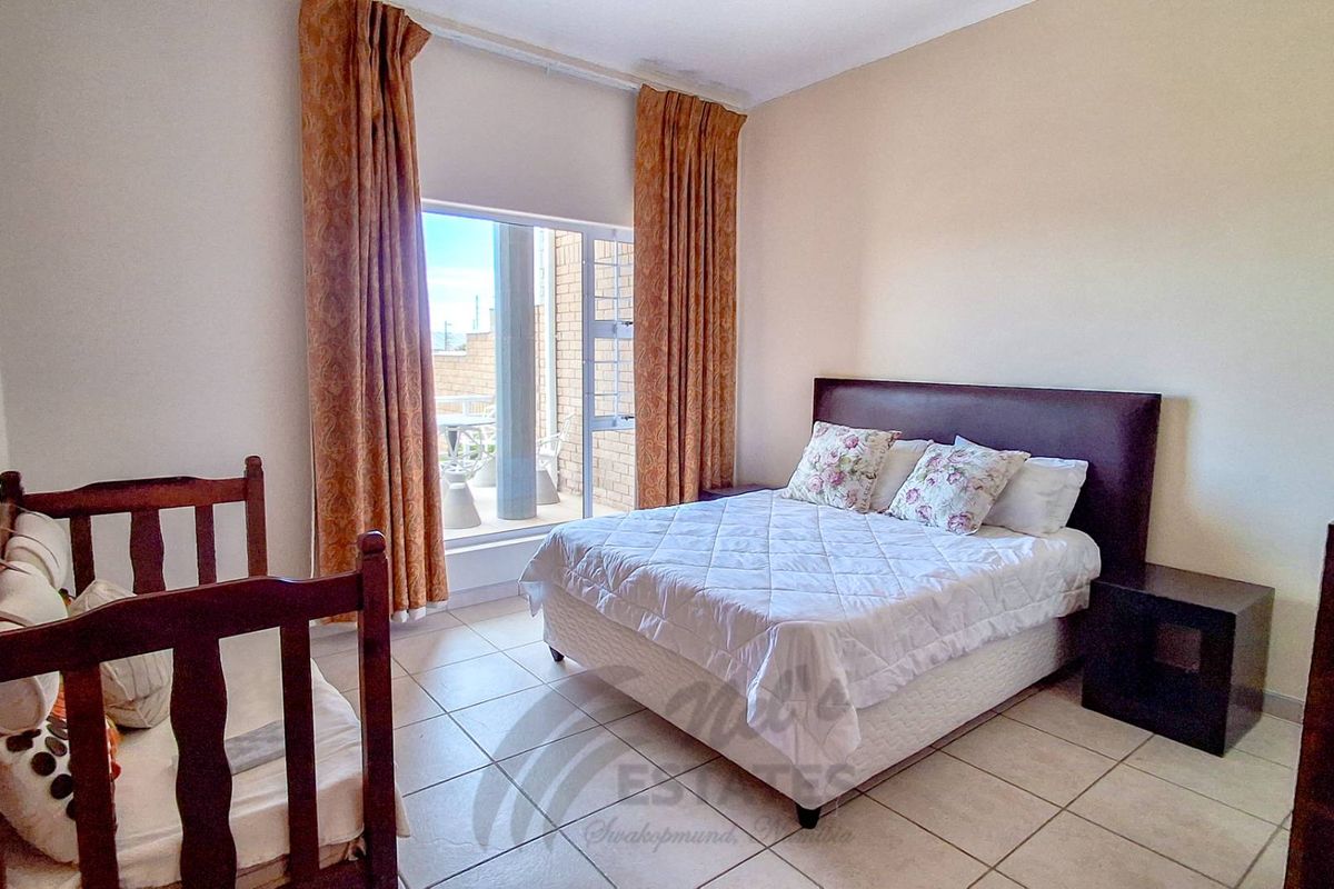 A well-lit bedroom featuring tiled flooring and direct access to a private balcony through a large glass sliding door.