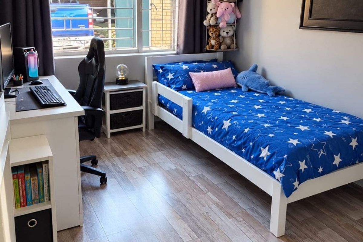 A well-maintained bedroom featuring durable laminate flooring, large windows with security bars, and neutral wall finishes, providing a comfortable and functional living space.