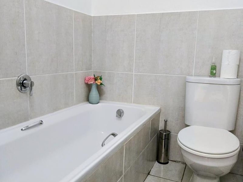 A functional bathroom featuring a built-in bathtub with chrome fixtures and a standard toilet, finished with neutral wall and floor tiling.