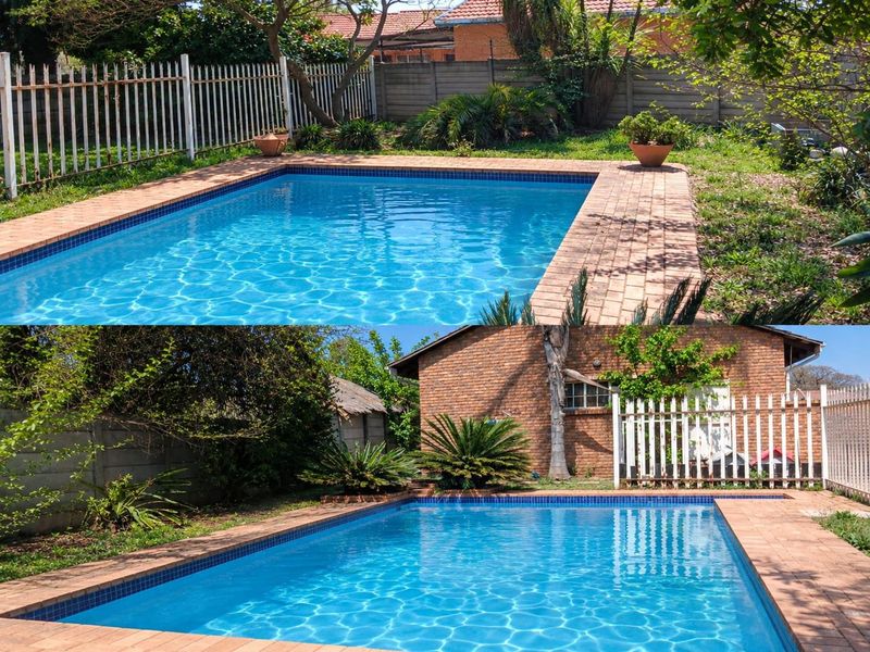 Outdoor pool area featuring a rectangular swimming pool with brick coping, surrounded by a garden, metal fencing, and brick boundary walls.