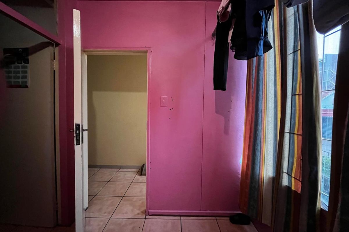 A bedroom featuring tiled flooring and a doorway leading to an adjacent space, with visible wall damage requiring repair and repainting.