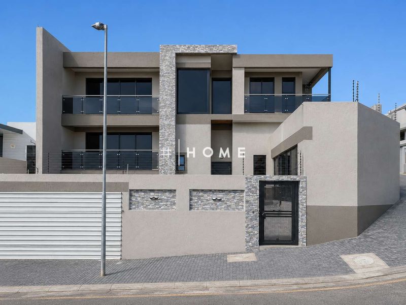Modern double-storey residence featuring contemporary stone cladding, glass balustrades, secure electric fencing, and a paved driveway with an automated garage.