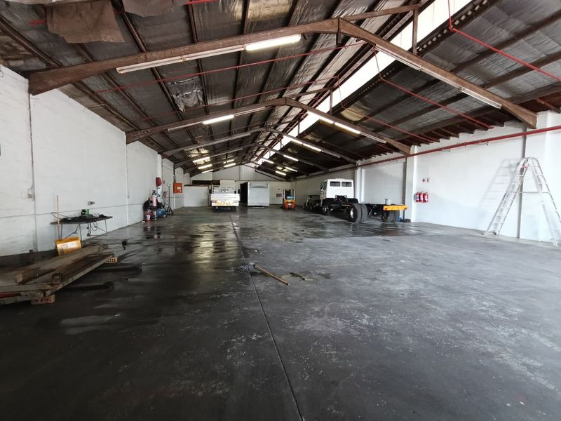Spacious industrial warehouse featuring high ceilings with exposed steel trusses, concrete flooring, and integrated fire safety equipment.