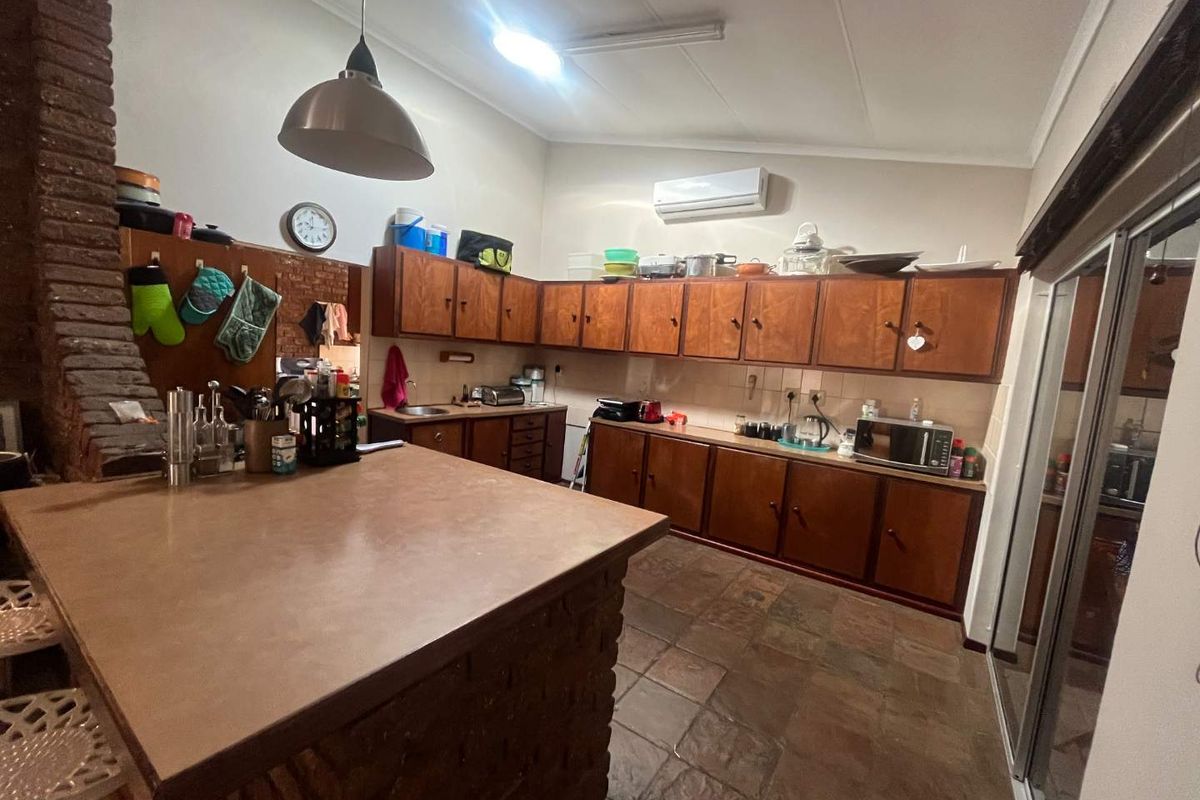 A functional kitchen featuring extensive wooden cabinetry, a central brick island, and durable tiled flooring, offering a classic layout with potential for modern updates.