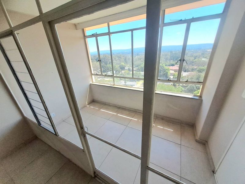 An enclosed balcony featuring tiled flooring and large aluminium-framed windows offering expansive views, providing a versatile space for a sunroom or study area.