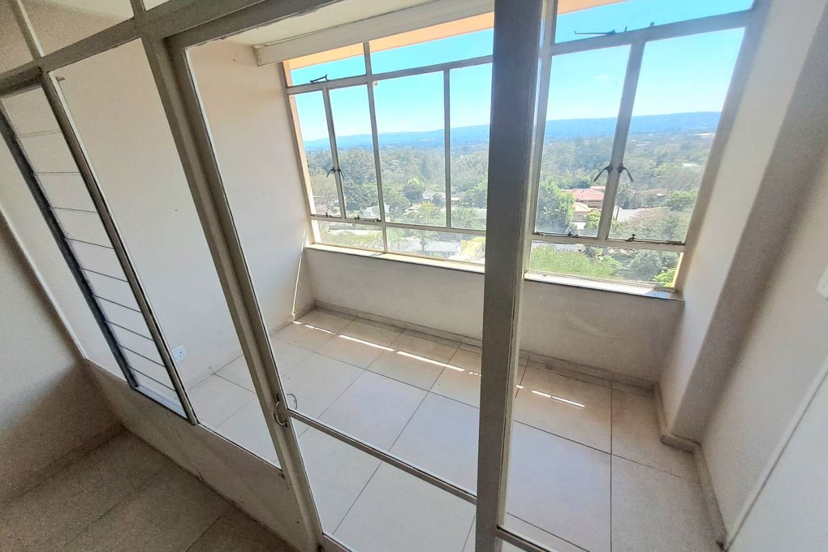 An enclosed balcony featuring tiled flooring and large aluminium-framed windows offering expansive views, providing a versatile space for a sunroom or study area.