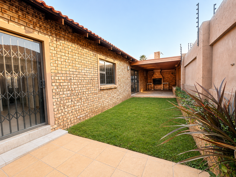 A well-maintained rear garden featuring a paved patio, built-in braai area, and secure perimeter wall with electric fencing.