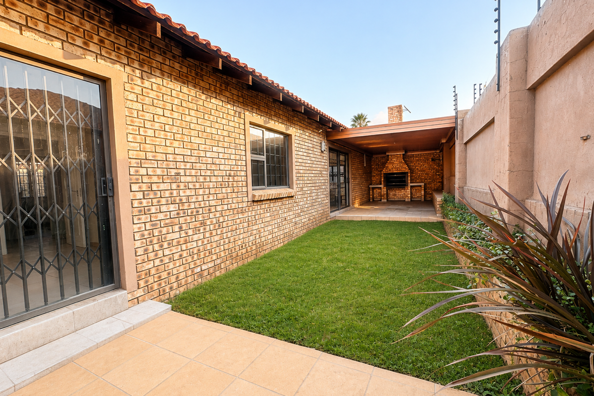 A well-maintained rear garden featuring a paved patio, built-in braai area, and secure perimeter wall with electric fencing.