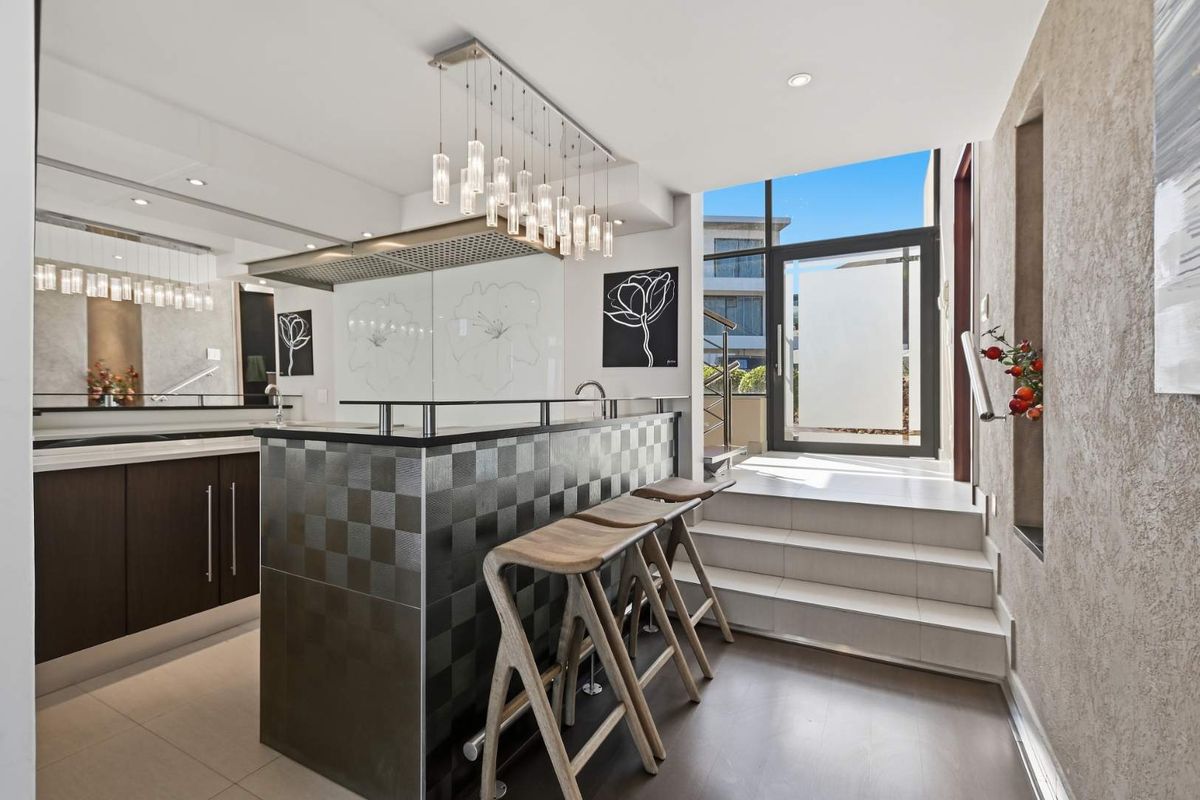 Modern kitchen featuring a sleek island with bar seating, high-end finishes, recessed lighting, and direct access to an outdoor area via a glass door.