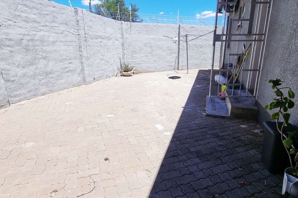A paved rear courtyard area featuring a high boundary wall with security fencing and direct access to the property.