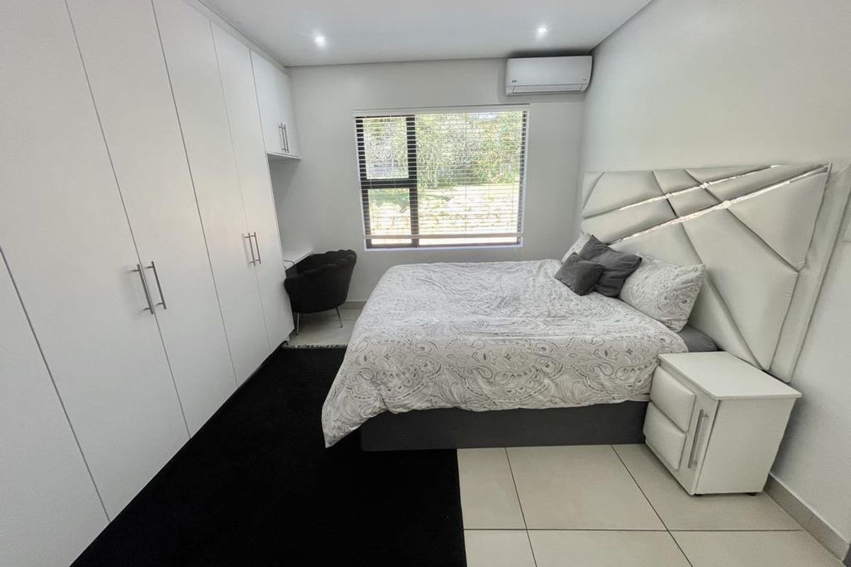 A modern bedroom featuring extensive built-in floor-to-ceiling cabinetry, a wall-mounted air conditioning unit, and large format floor tiles.