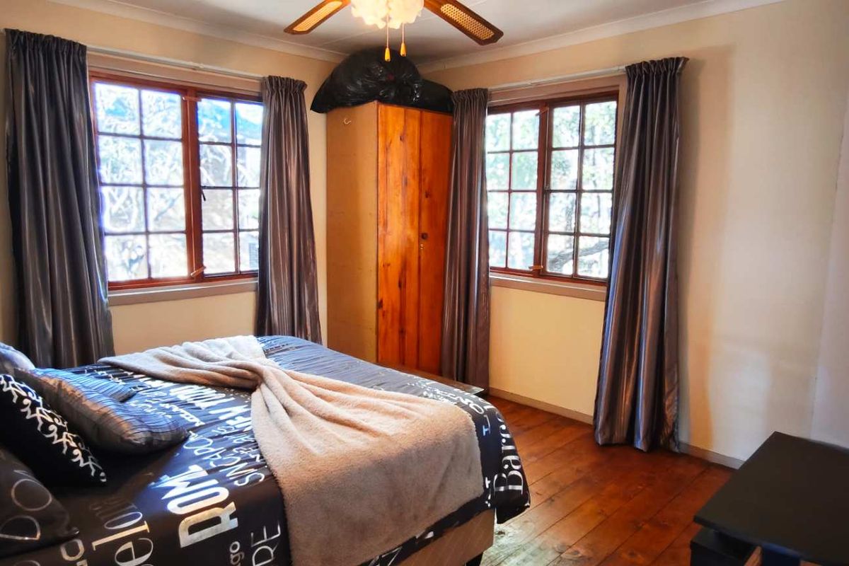 A bedroom featuring timber flooring, dual windows with natural light, and a ceiling fan.