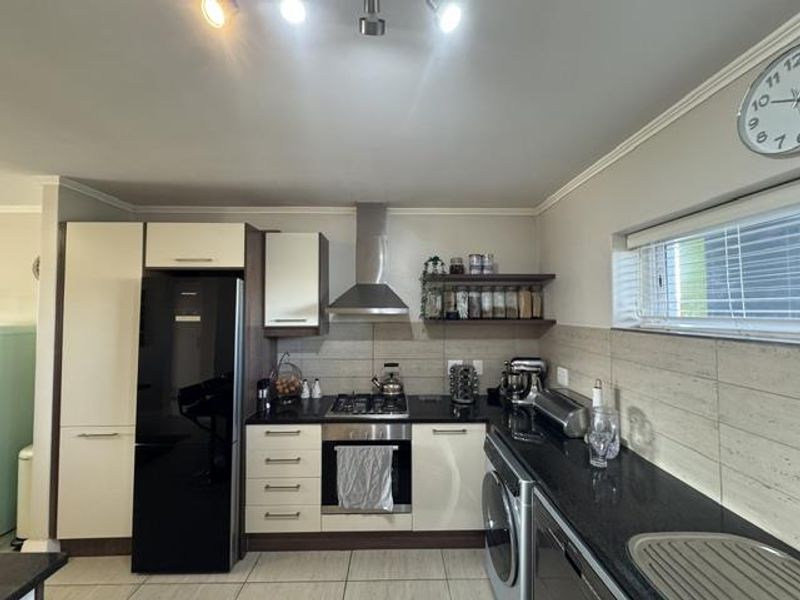 A functional kitchen featuring modern two-tone cabinetry, granite countertops, a stainless steel extractor fan, and a built-in oven with gas hob.