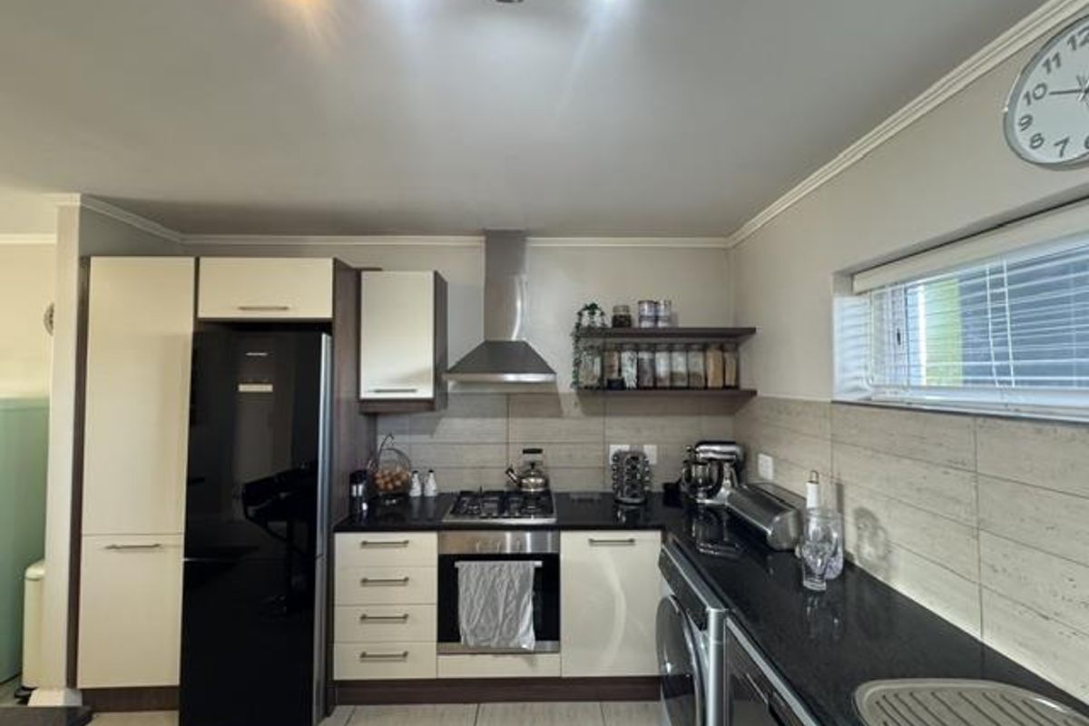 A functional kitchen featuring modern two-tone cabinetry, granite countertops, a stainless steel extractor fan, and a built-in oven with gas hob.