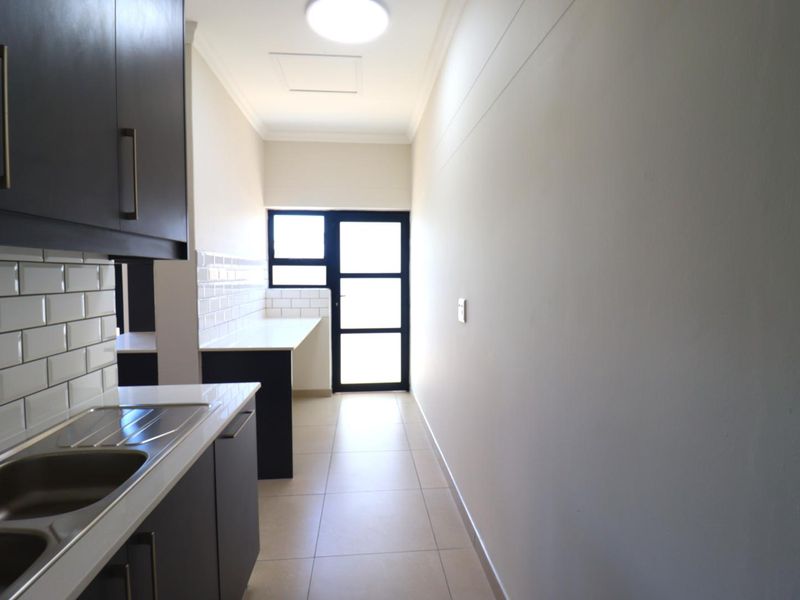 A clean and functional scullery featuring dark cabinetry, white subway tile backsplash, stone countertops, and direct access to the exterior.