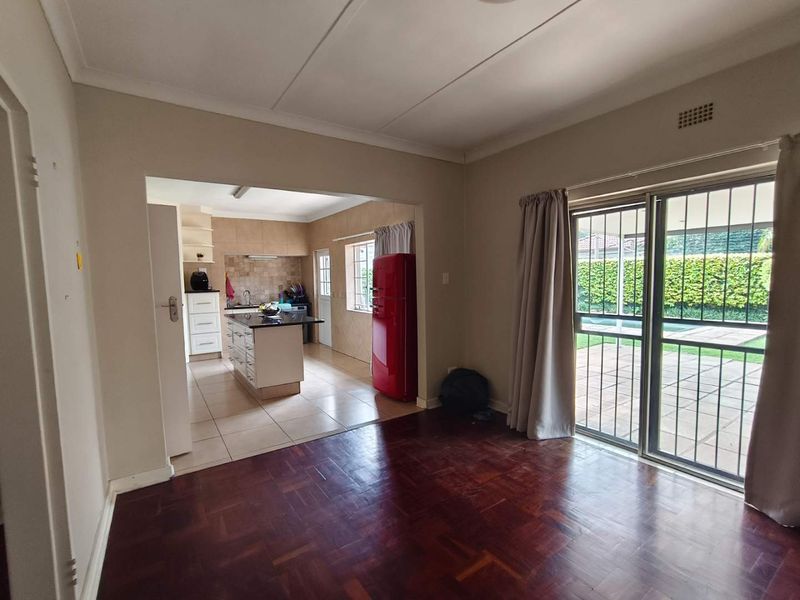 Open plan living area featuring parquet flooring, flowing into a kitchen with a central island and tiled floors, with sliding door access to the patio.