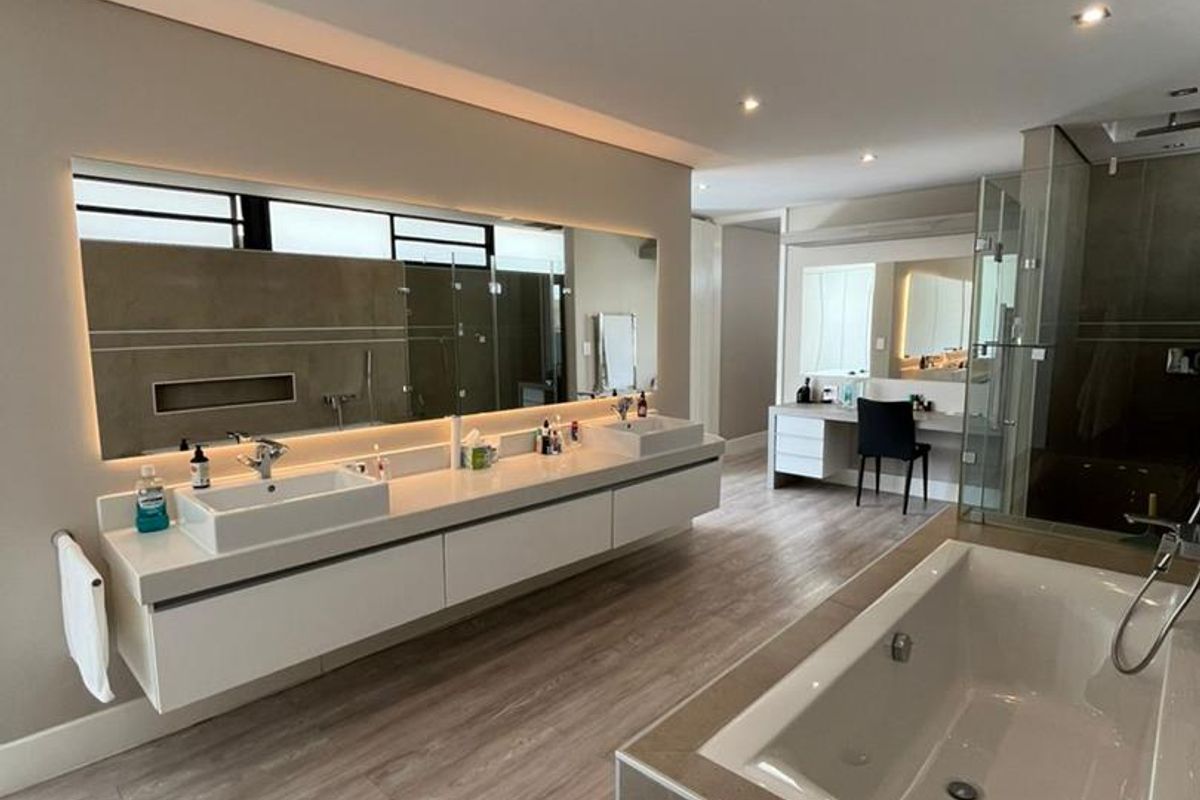 Modern, spacious bathroom featuring a double vanity with backlit mirror, built-in bathtub, glass-enclosed shower, and integrated dressing area with high-quality finishes.
