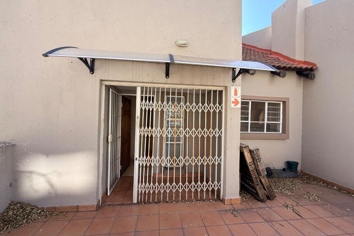 Exterior view of an apartment entrance featuring a tiled patio, protective awning, and a security gate over the main doorway.