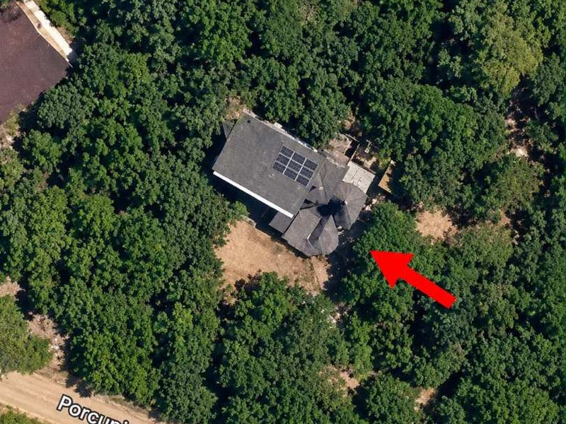Aerial view of a residential property nestled in a wooded area, featuring a roof equipped with solar panels.