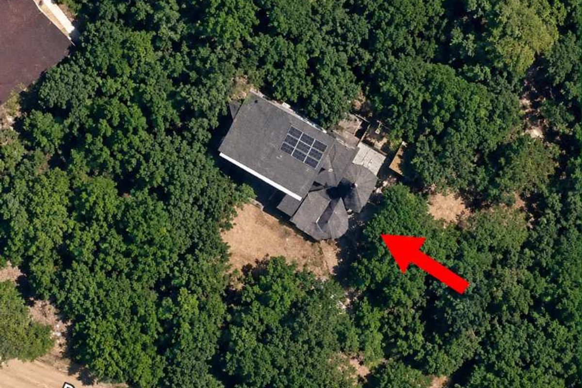 Aerial view of a residential property nestled in a wooded area, featuring a roof equipped with solar panels.