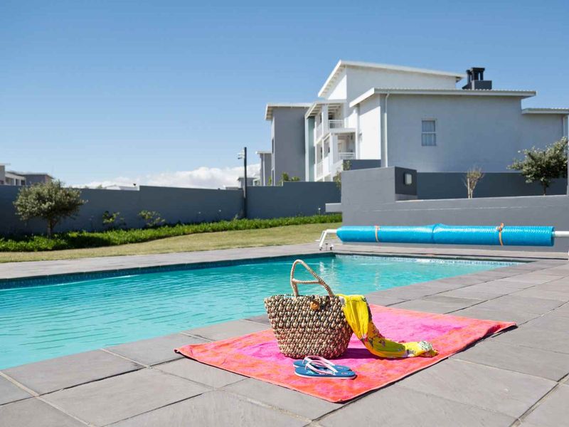 A well-maintained outdoor swimming pool area featuring a paved deck, boundary wall, and a pool cover, set against a modern apartment building.