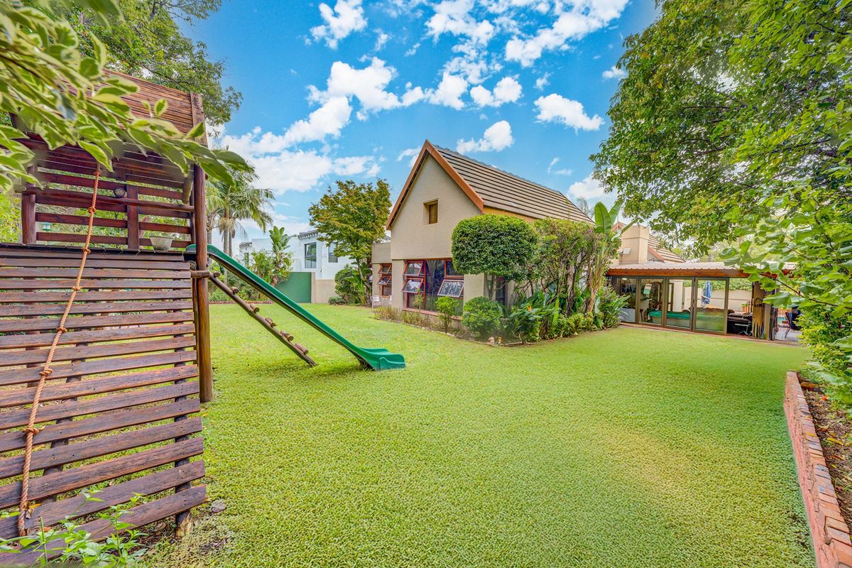 A spacious rear garden featuring a well-maintained lawn, mature trees, and a covered patio area attached to the main house structure.