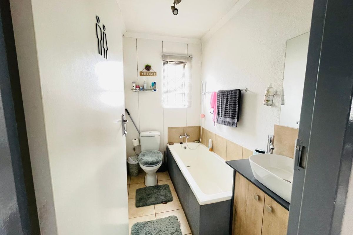 A functional bathroom featuring a bathtub, a modern vessel sink with vanity cabinetry, and a toilet.