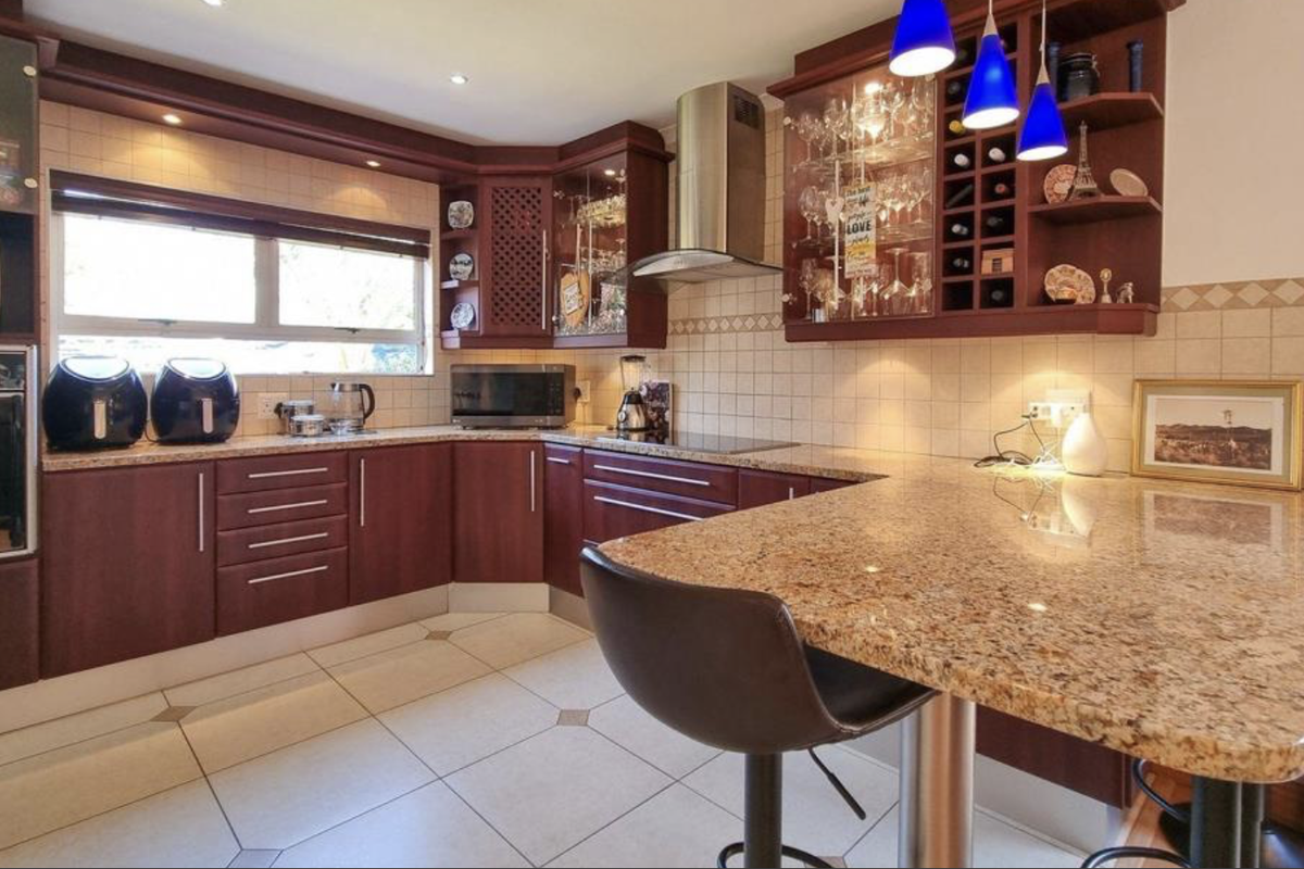 A well-appointed kitchen featuring dark wood cabinetry, granite countertops, a breakfast bar, and integrated appliances with a tiled backsplash and under-cabinet lighting.