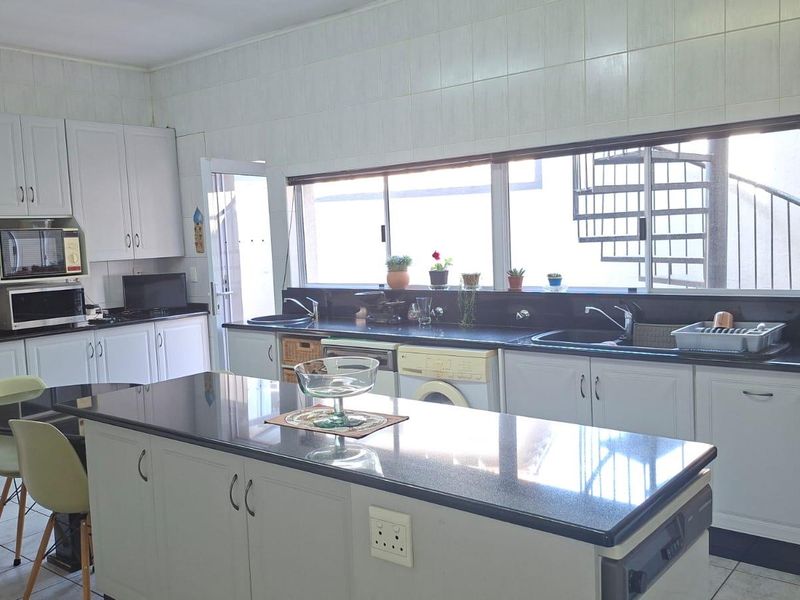 Spacious kitchen featuring white cabinetry, dark granite countertops, a central island, and tiled finishes, offering a functional layout with ample workspace.