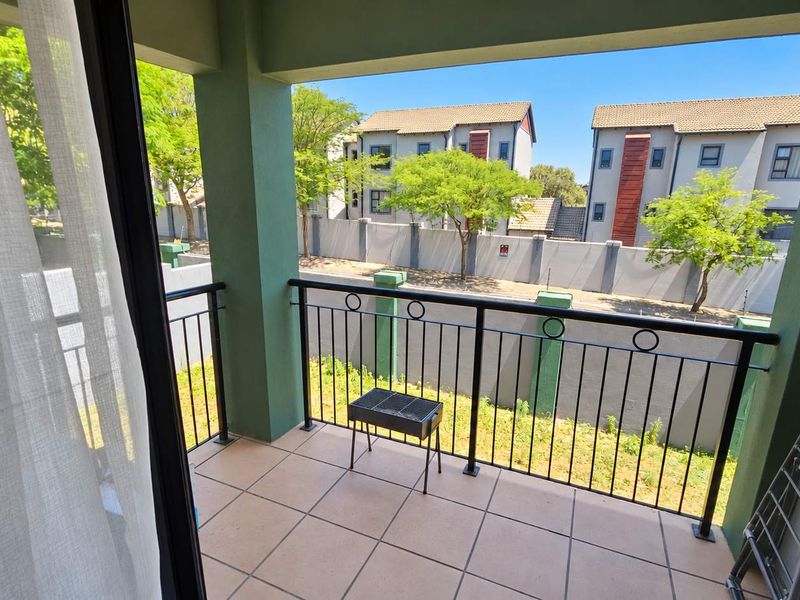 A covered balcony featuring tiled flooring and a metal balustrade, offering an outdoor space with views of the surrounding complex.