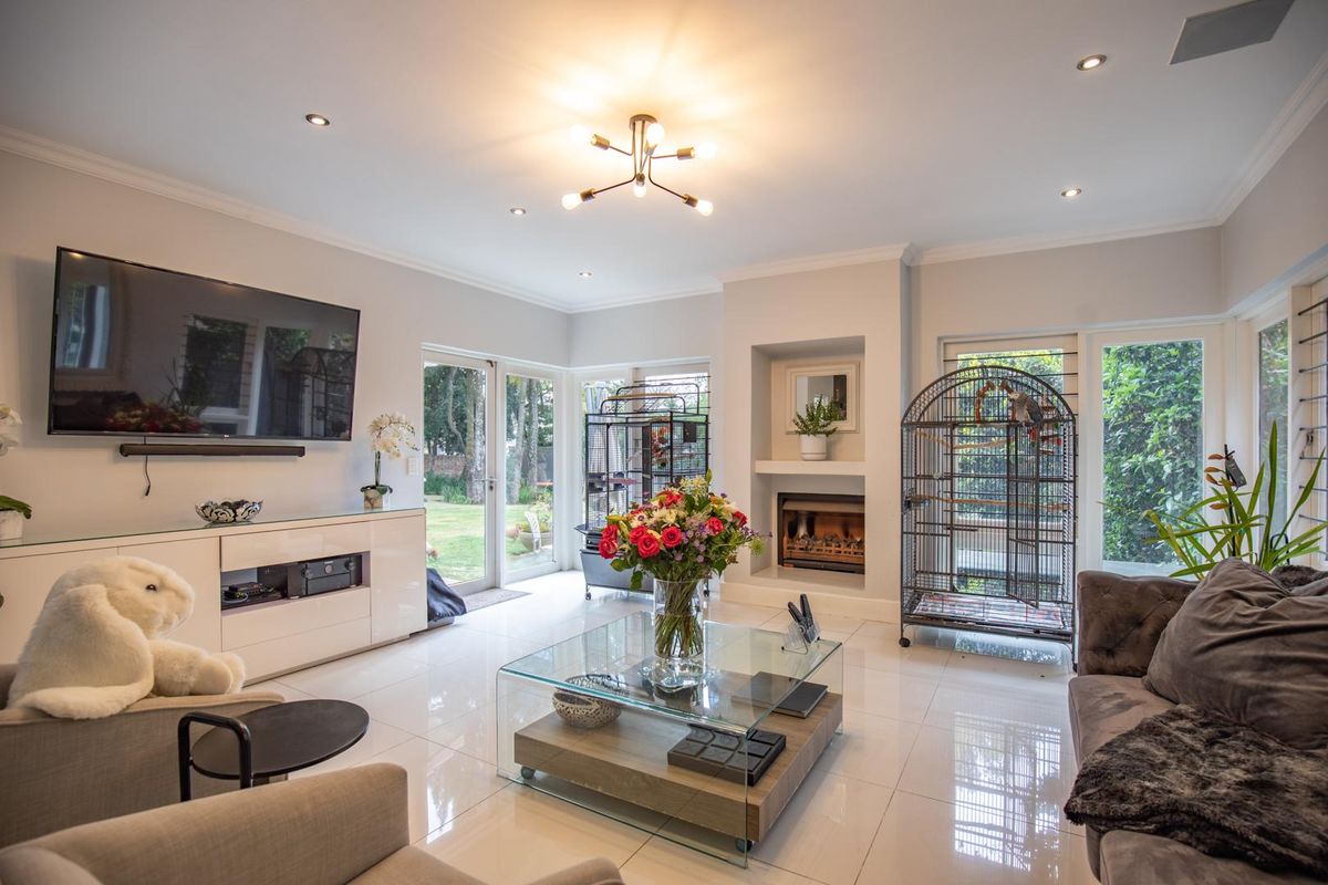 Bright and spacious living room featuring large glass doors, polished tile flooring, and a built-in fireplace, offering seamless access to the garden.