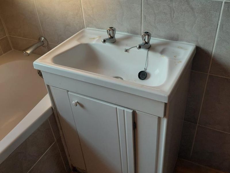 A compact bathroom featuring a vanity cabinet with a ceramic basin, dual taps, and an adjacent bathtub with tiled walls and flooring.