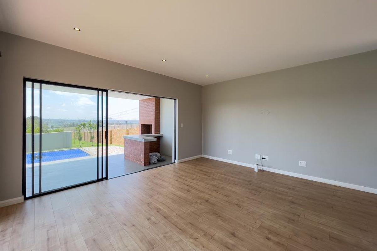 Spacious living area featuring modern wood-look flooring, recessed lighting, and large sliding glass doors opening onto a covered patio with a built-in brick braai.
