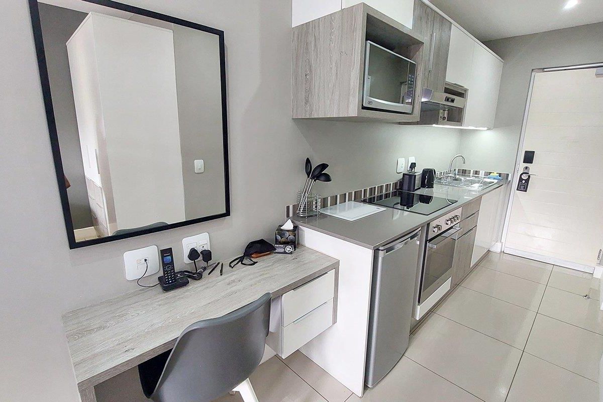 Modern compact kitchen featuring built-in cabinetry, integrated appliances including a hob and oven, and a convenient built-in desk area with tiled flooring.