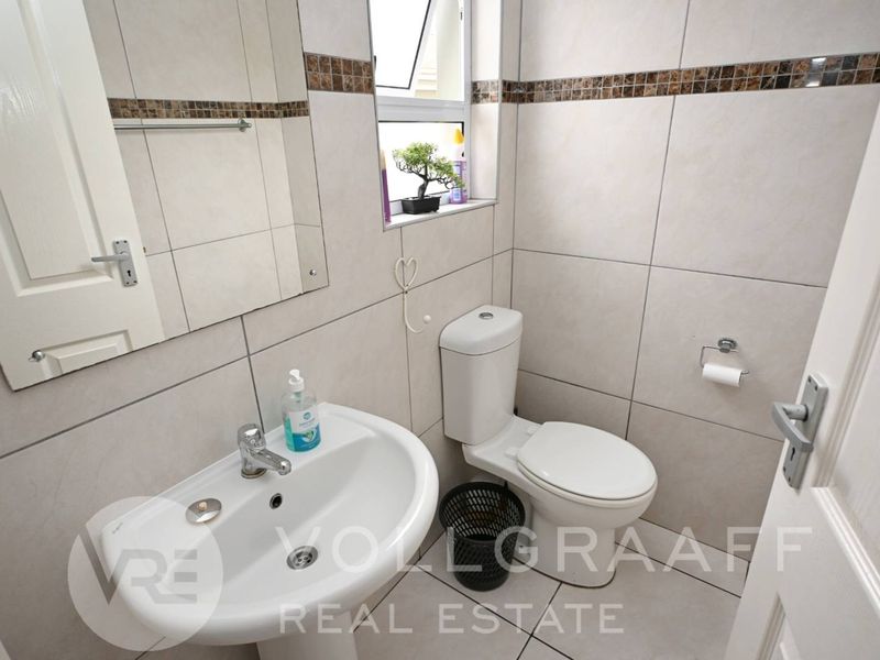 A compact, well-maintained bathroom featuring neutral wall and floor tiles, a pedestal basin, and a standard toilet.