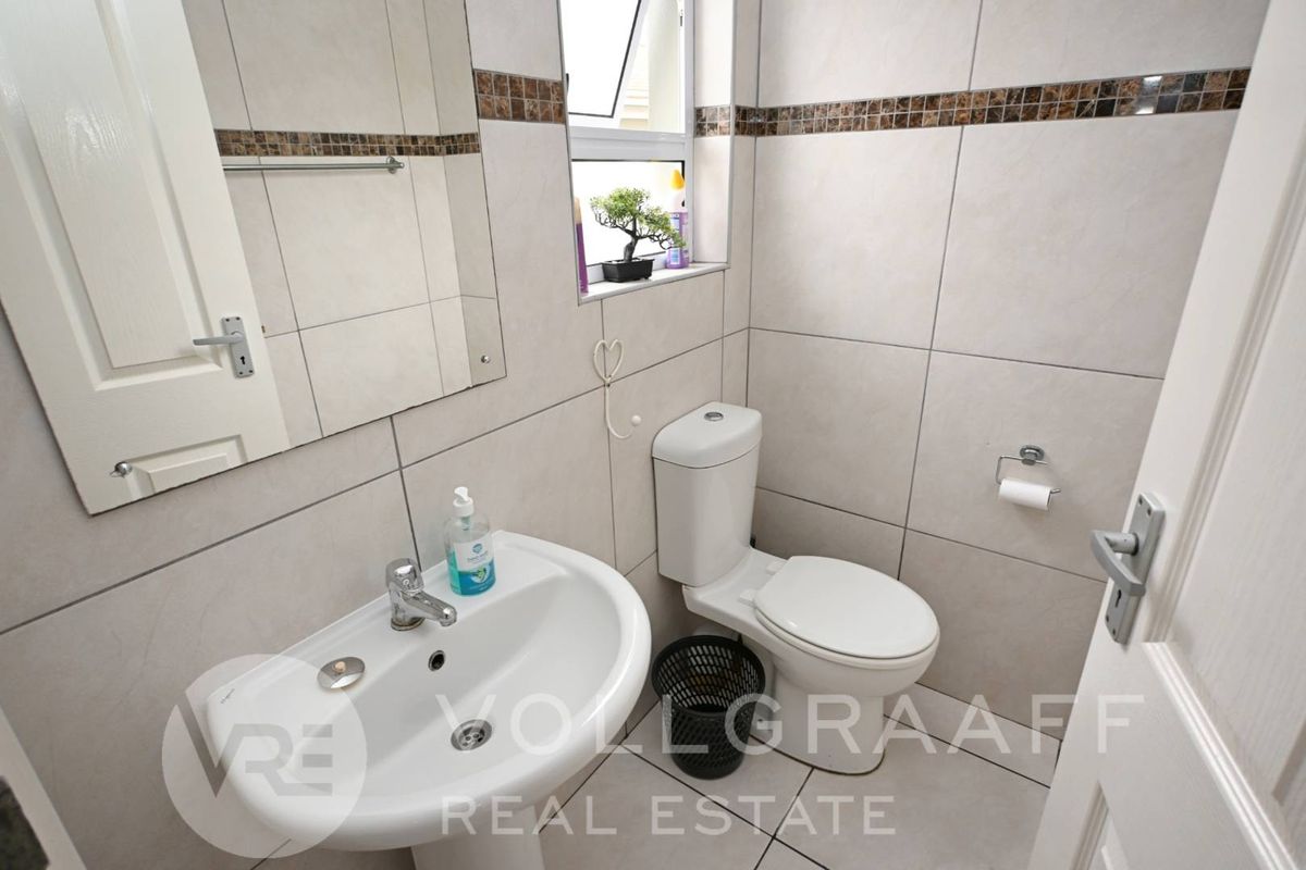 A compact, well-maintained bathroom featuring neutral wall and floor tiles, a pedestal basin, and a standard toilet.