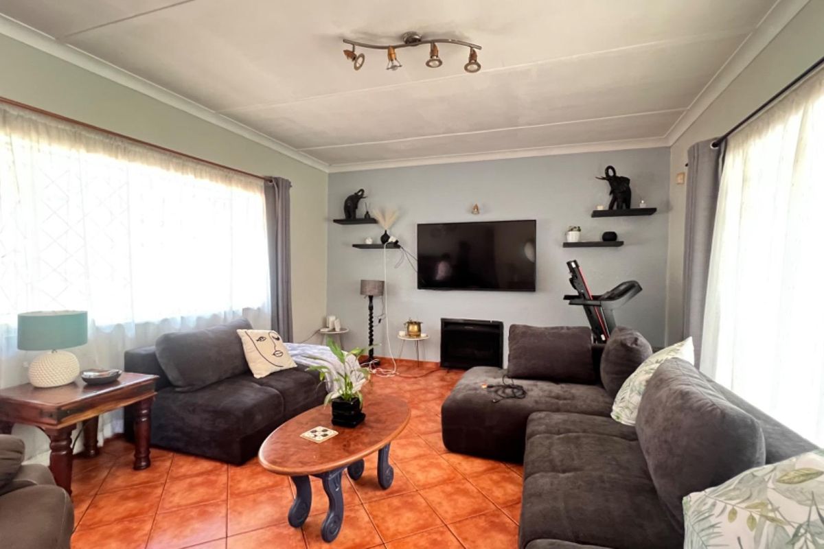 A comfortable living room featuring terracotta floor tiles, a built-in fireplace, and dual aspect windows providing ample natural light.