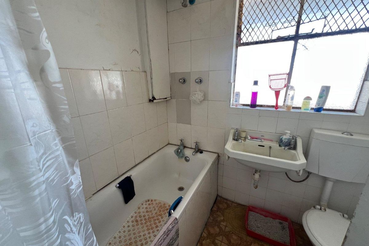 A dated bathroom featuring a bathtub, wall-mounted basin, and toilet, requiring significant renovation and cosmetic updates to improve its condition and functionality.
